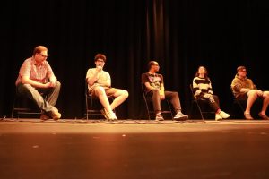 A photo of a five-person panel on a darkened stage