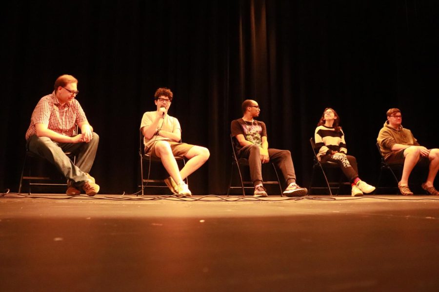 A photo of a five-person panel on a darkened stage