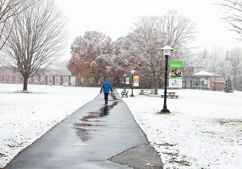 Student walking on pathway away from camera across snowy quad